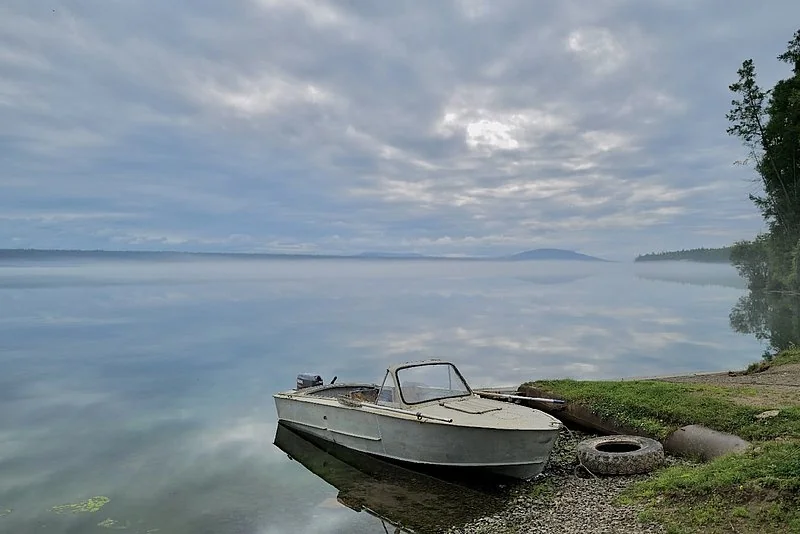A boat and shore in the local-history account, captioned as the waters covering Dubynino’s historical site. This is a modern landscape, not a pre-relocation view of the village.