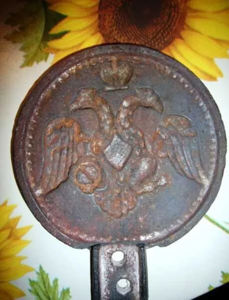A museum object illustrating the Nikolaevsky works history: a cast-iron waffle maker bearing a raised double-headed eagle. The photograph shows an artefact rather than an operating factory.